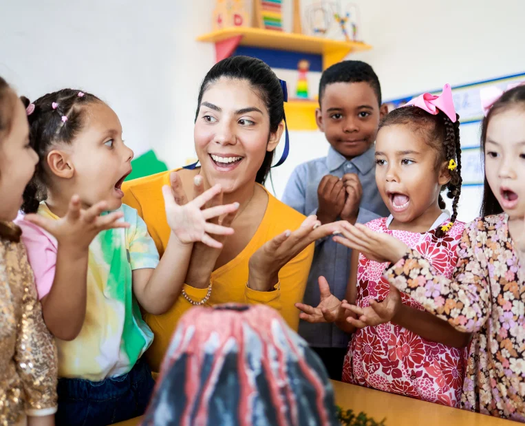 Educator with children in a classroom, hands raised